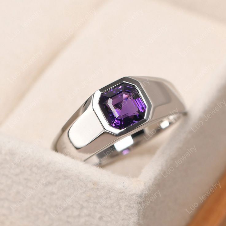 a ring with a purple stone in it sitting on a white velvet box that is open