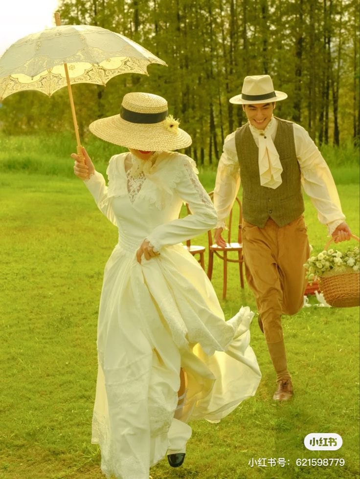 a man and woman walking in the grass with an umbrella over their heads, holding hands