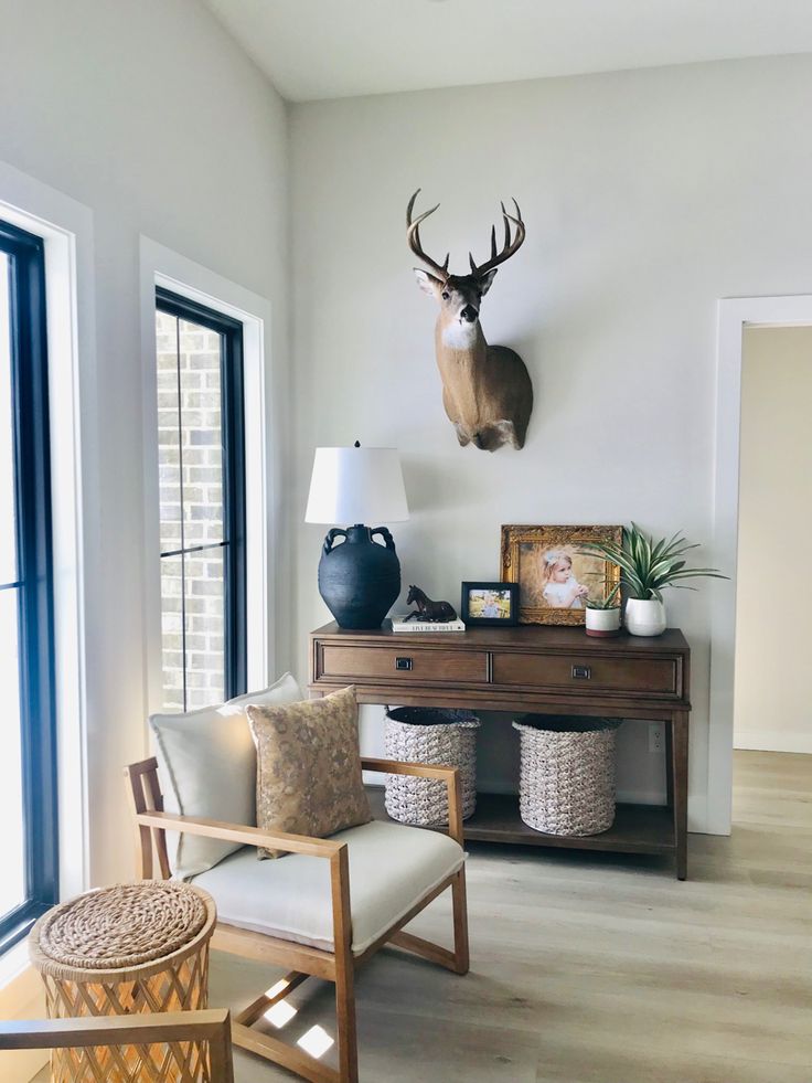 a deer head mounted on the wall above a desk with two chairs and a lamp