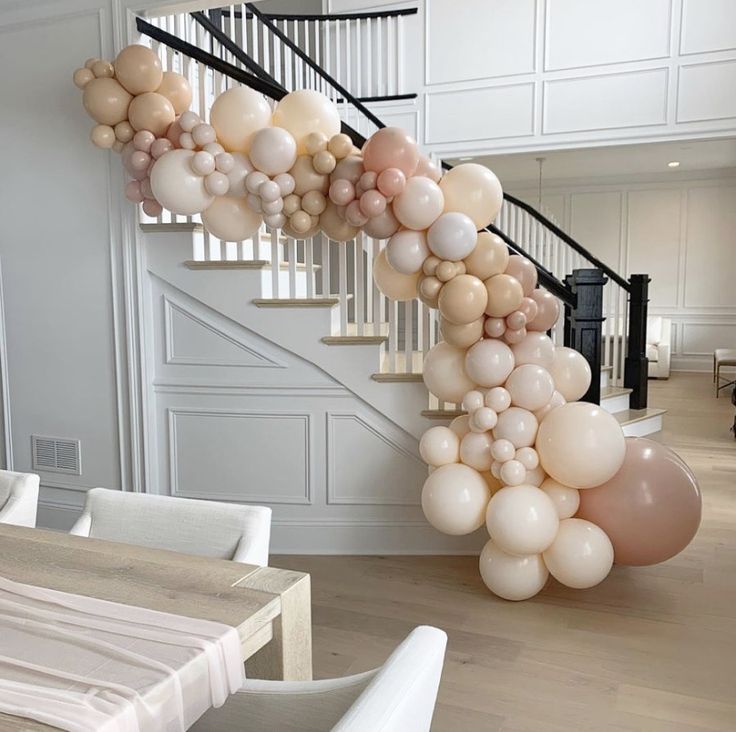 a bunch of balloons hanging from the side of a spiral staircase in a house with white walls and wooden floors