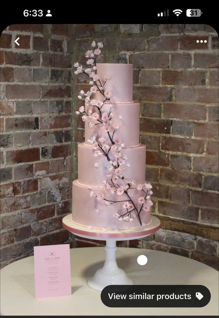 a three tiered cake with pink frosting and flowers on the top is displayed in front of a brick wall