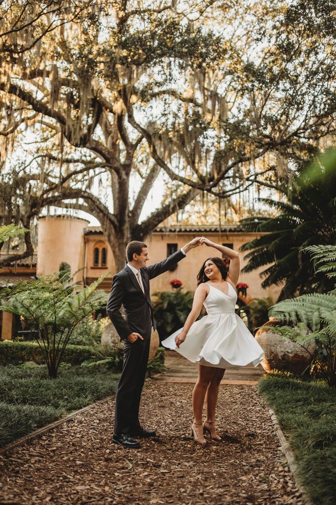 a man and woman dancing together in front of some trees with spanish moss on the ground