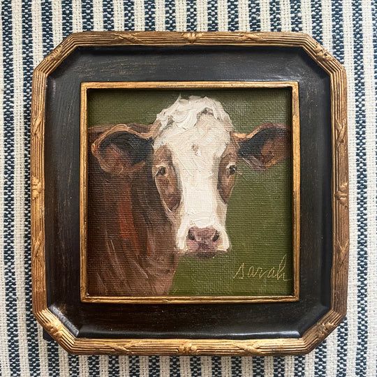 a painting of a cow in a frame on a striped cloth background with the word animal written below it