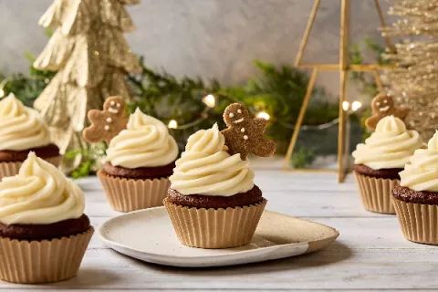 cupcakes with white frosting and brown icing on a plate next to christmas decorations