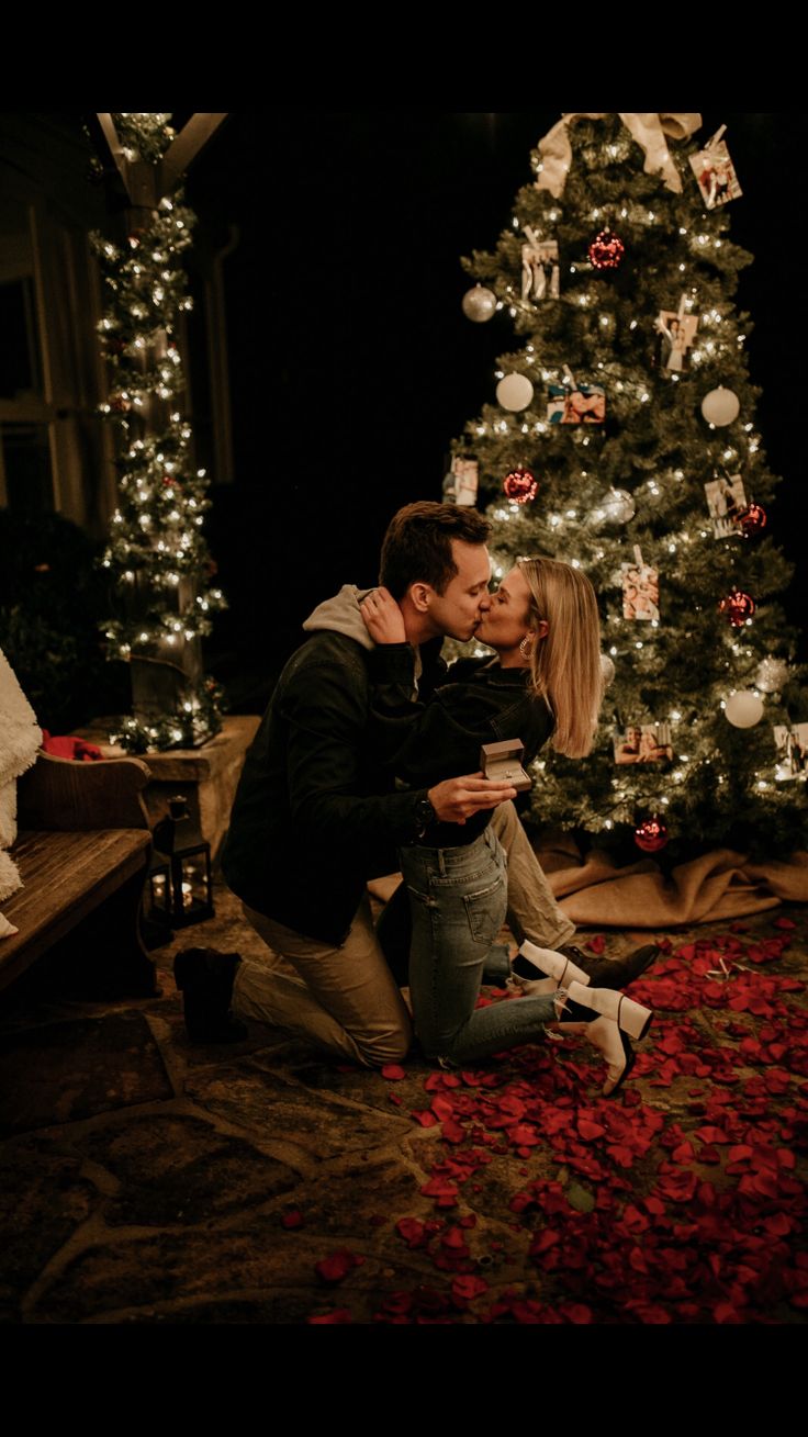 a man and woman kissing in front of a christmas tree with presents on the floor