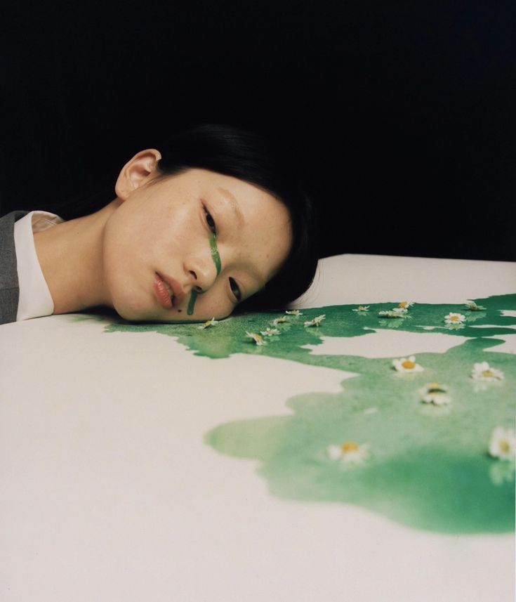 a woman laying on top of a bed with her head resting on the table next to flowers