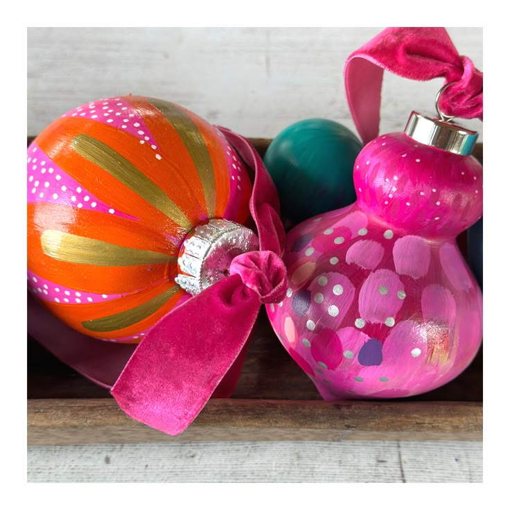 three colorful ornaments are sitting on a wooden shelf with pink ribbon around them and one has a silver ornament in the middle