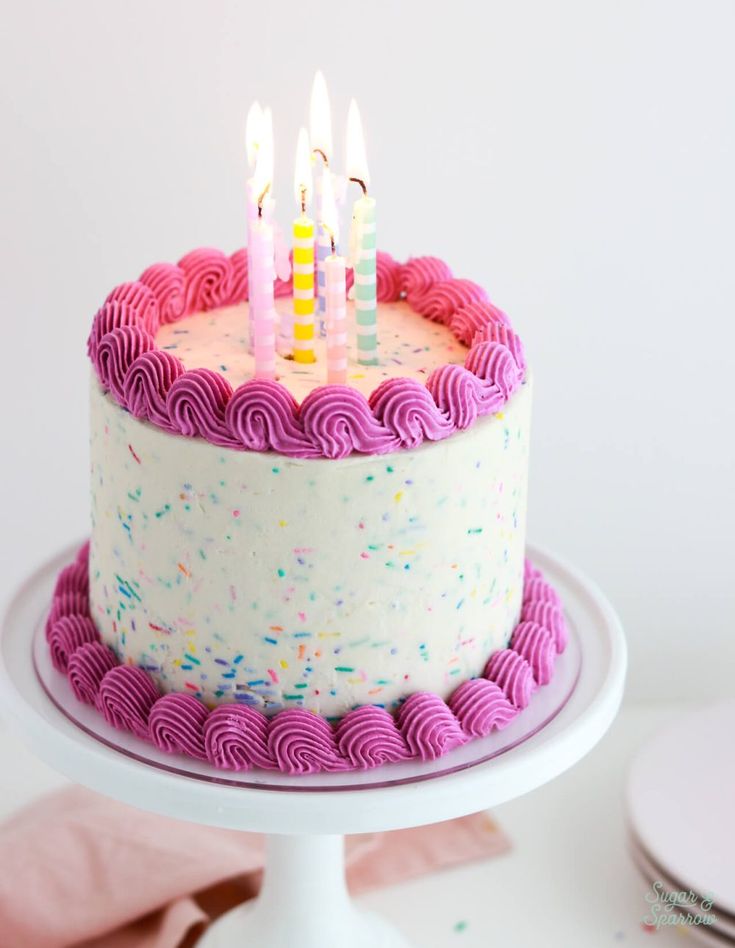 a birthday cake with pink frosting and lit candles on top, sitting on a white pedestal