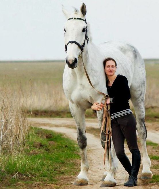 a woman standing next to a white horse on a dirt road