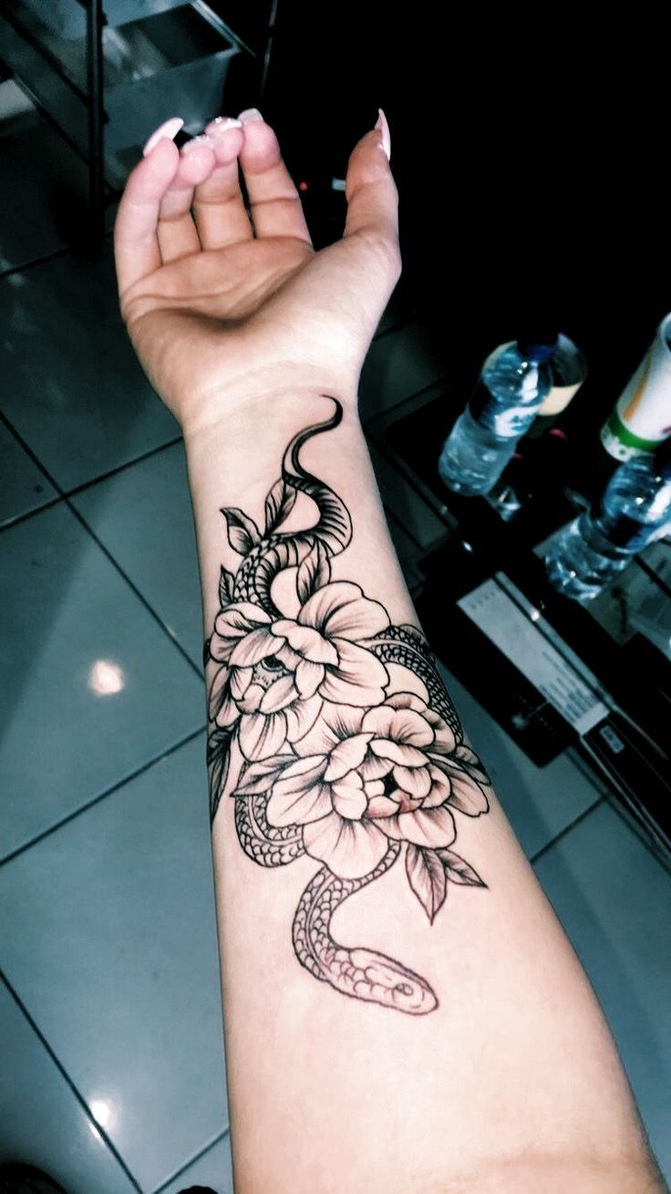 a woman's arm with a snake and flowers tattoo on it