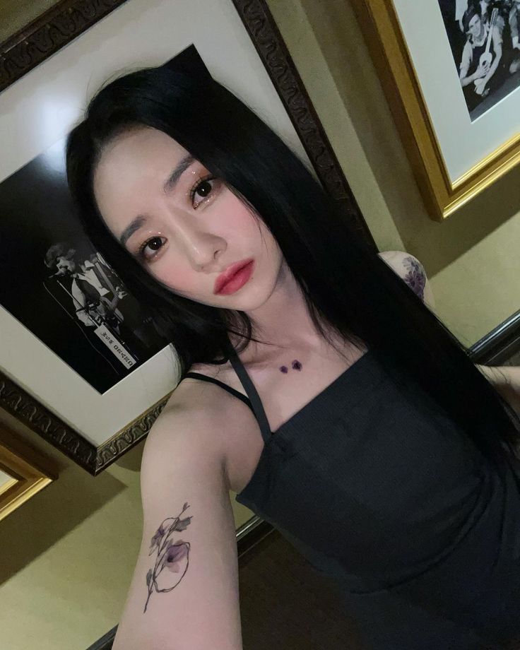 a woman with long black hair and tattoos on her arm, posing for the camera