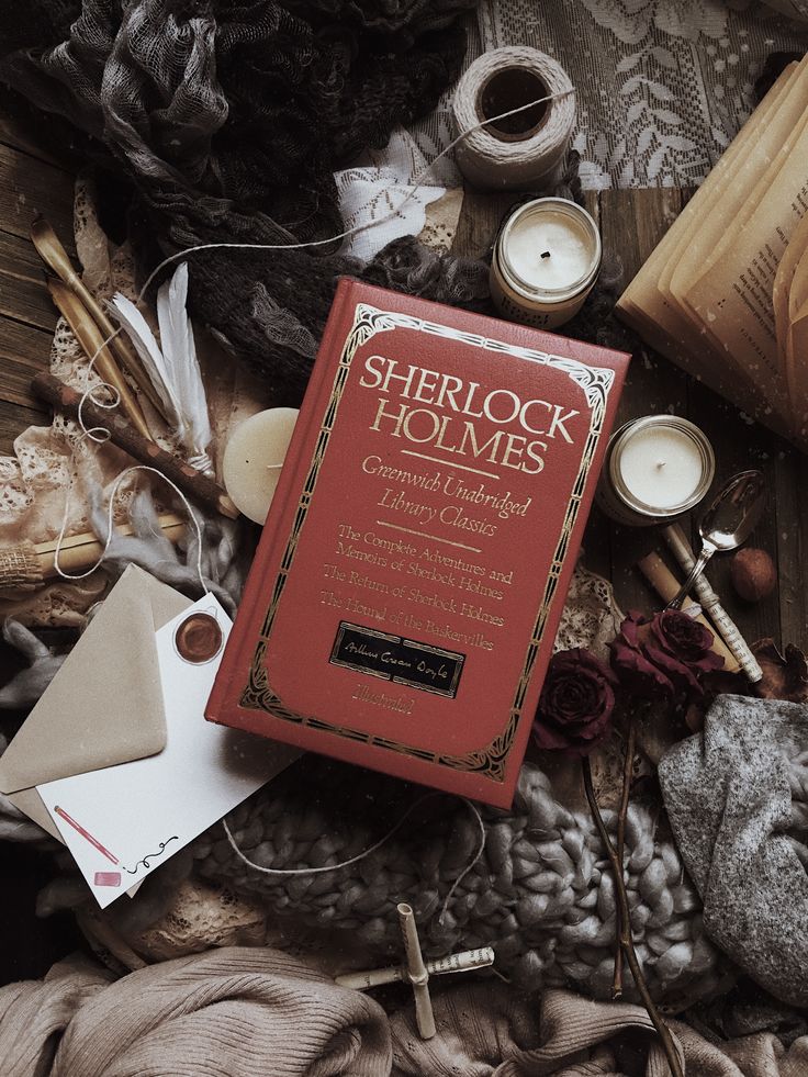 a red book sitting on top of a pile of cloth next to candles and other items