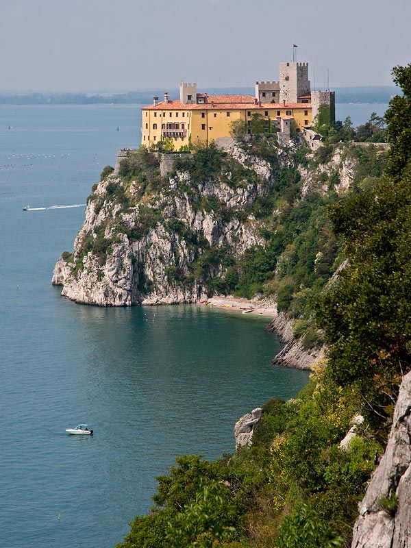 an old castle sits on top of a cliff overlooking the ocean with boats in the water