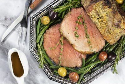 a plate with meat, olives and green beans on it next to a knife