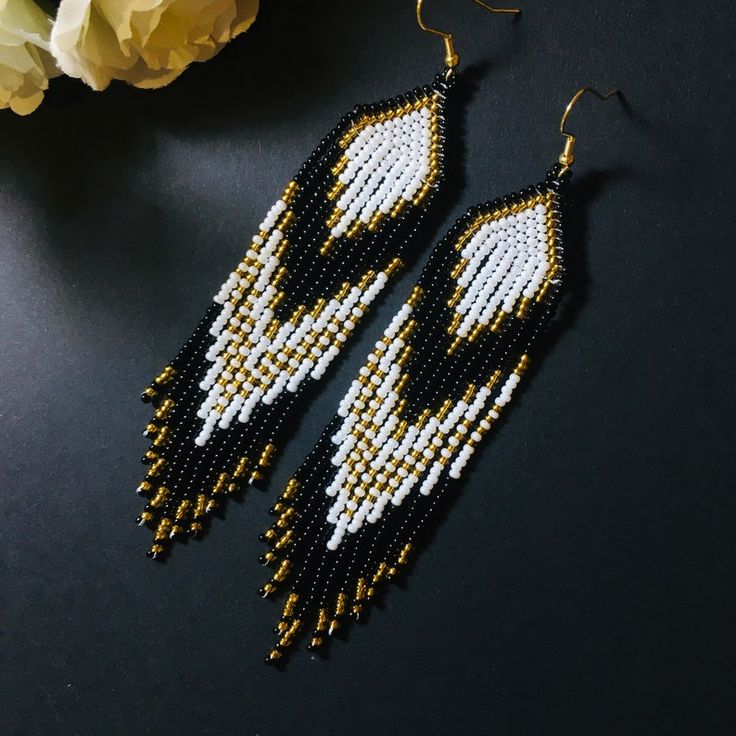 a pair of black and white beaded earrings next to a yellow flower on a table