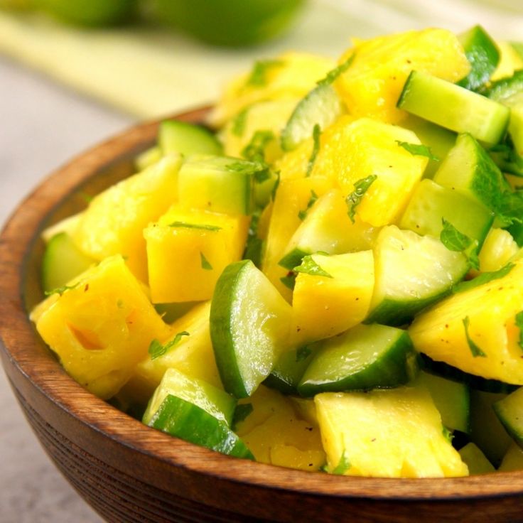 a wooden bowl filled with sliced cucumbers and limes on top of a table