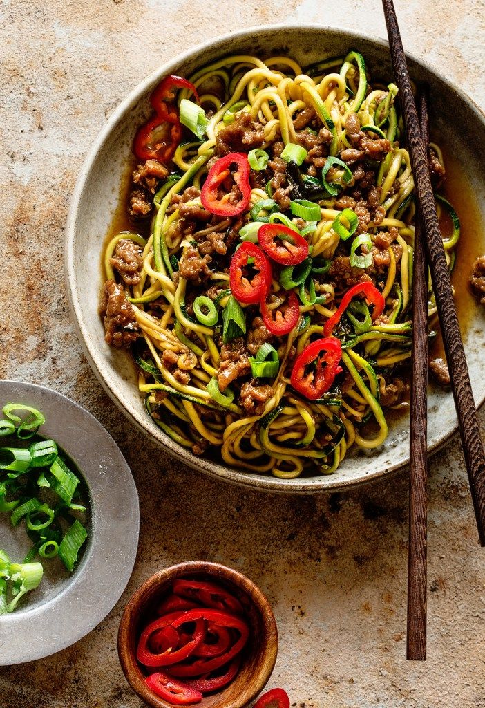 a bowl filled with noodles and vegetables next to chopsticks on a table top