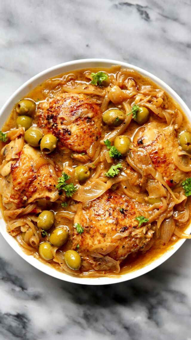 a white bowl filled with chicken and olives on top of a marble countertop