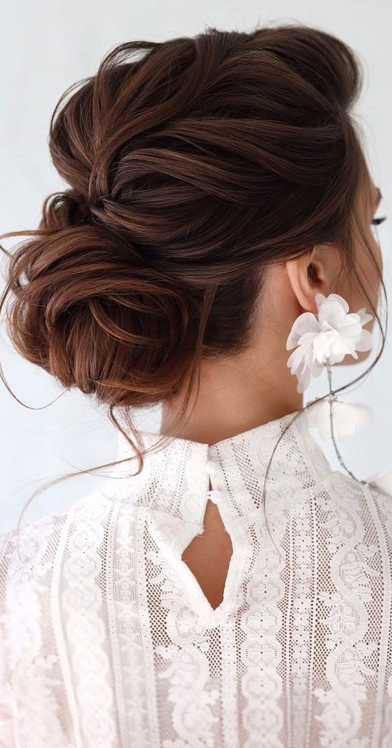 a woman with her hair in a low bun, wearing white blouse and flower clip earrings