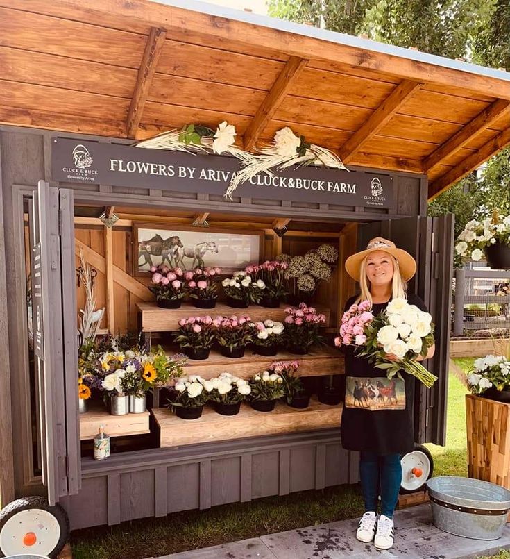 a woman standing in front of a flower stand with lots of flowers on the shelves