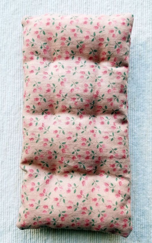 a pink and green flowered pillow on top of a blue sheet with white background