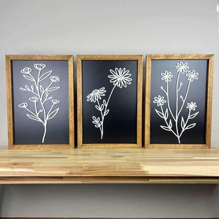 three black and white framed flowers on a wooden shelf