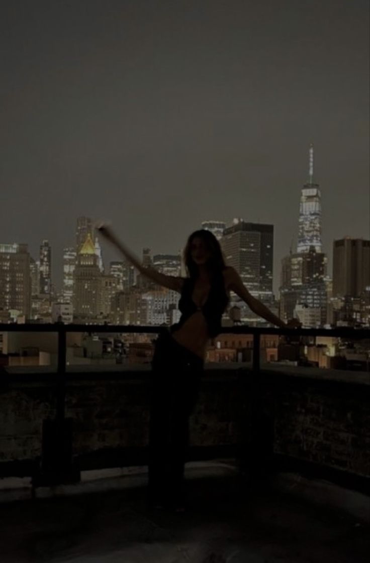 a woman standing on top of a roof in front of a city skyline at night