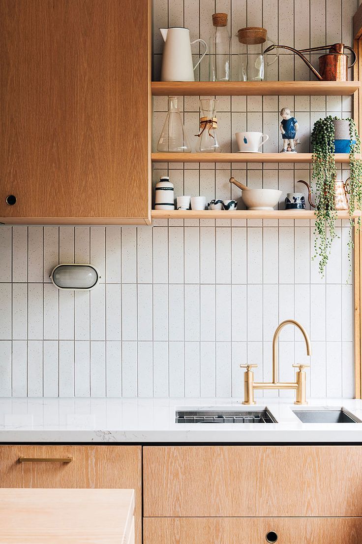 a kitchen with wooden cabinets and white tile backsplash, brass faucet