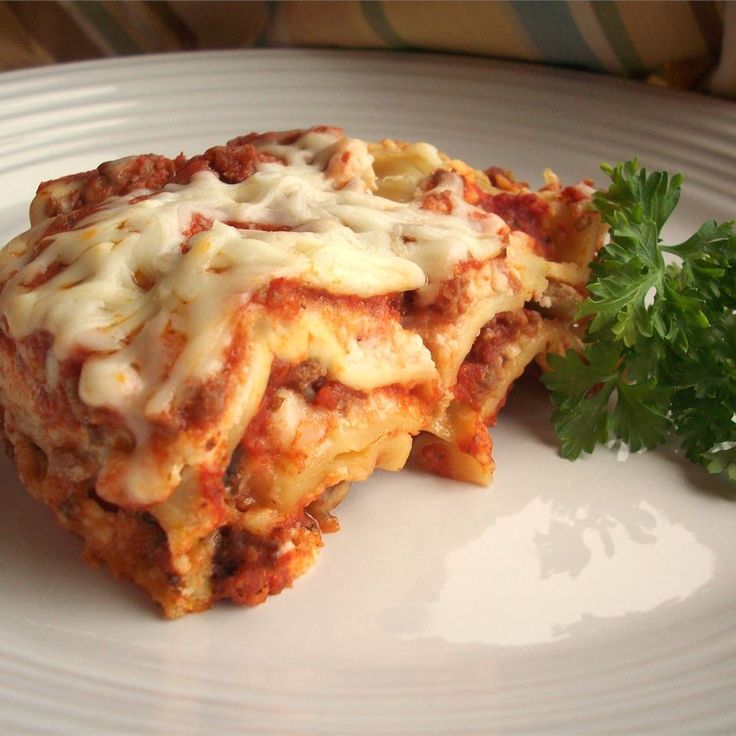 a white plate topped with lasagna covered in sauce and cheese next to a parsley