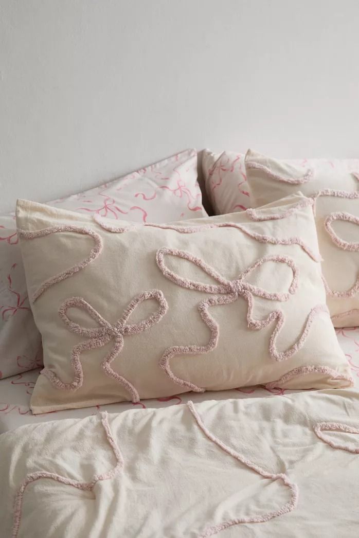 two pillows on top of a bed with white sheets and pink threadwork in the middle