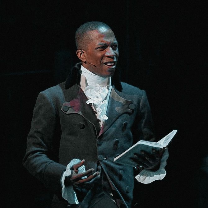 a man in a black suit and white shirt is holding a piece of paper while standing on stage