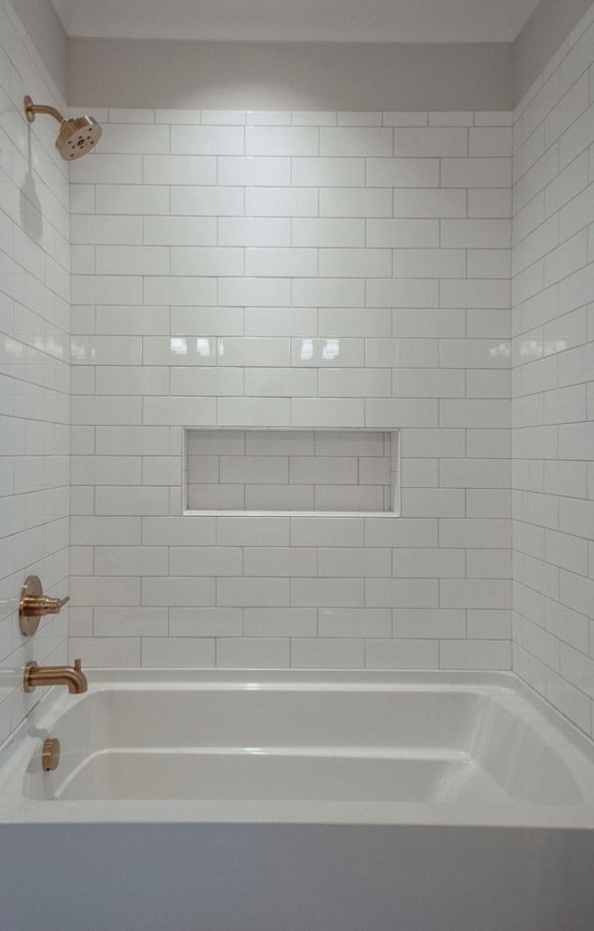 a bathroom with white tile and gold faucet handles on the shower head is shown