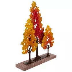 three trees with different colored leaves on top of a wooden base and one is standing in the middle