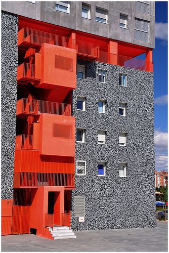 an orange and grey building with balconies on the top floor in front of it