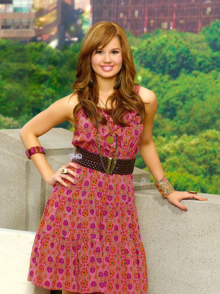 a beautiful young woman standing next to a cement wall with her hands on her hips