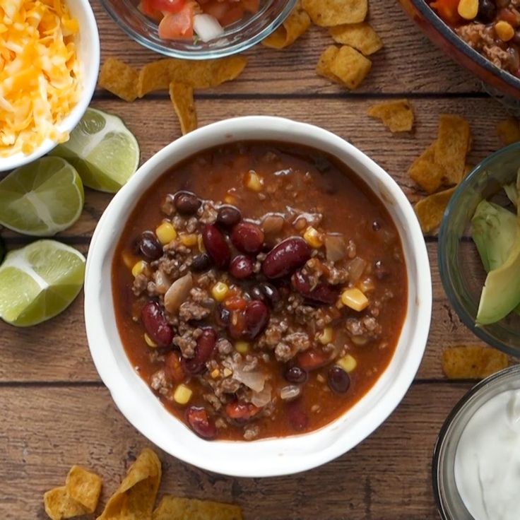 a table topped with bowls of chili, cheese and tortilla chips