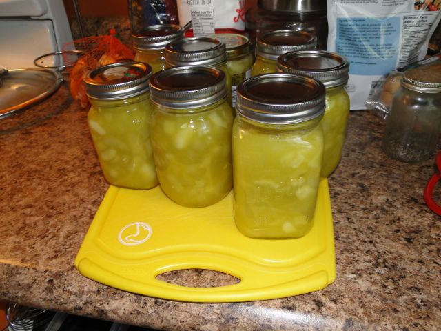 four jars filled with pickles sitting on top of a yellow tray next to a stove