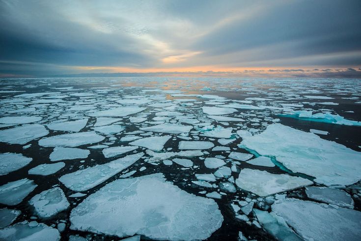 ice floes floating in the ocean with sun shining through cloudy clouds above them and blue water below