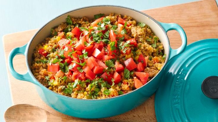 a pot filled with rice and vegetables on top of a wooden cutting board next to a spoon