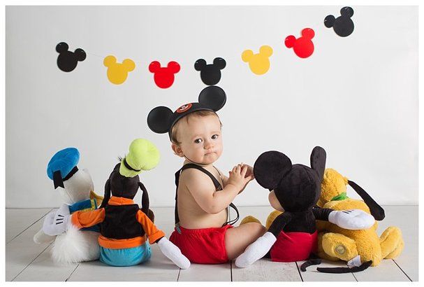 a baby sitting in front of mickey mouse stuffed animals