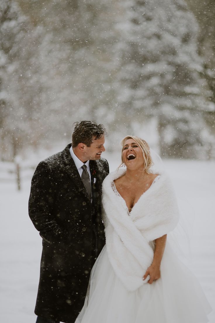 a bride and groom laughing in the snow