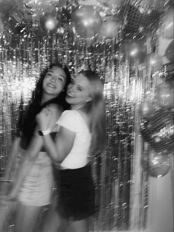 two young women standing next to each other in front of a disco ball wall with lights