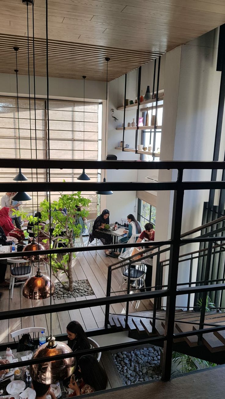 people are sitting at tables in a room with metal railings and potted plants