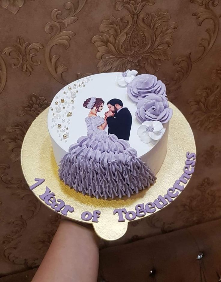 a hand holding a cake decorated with the bride and groom