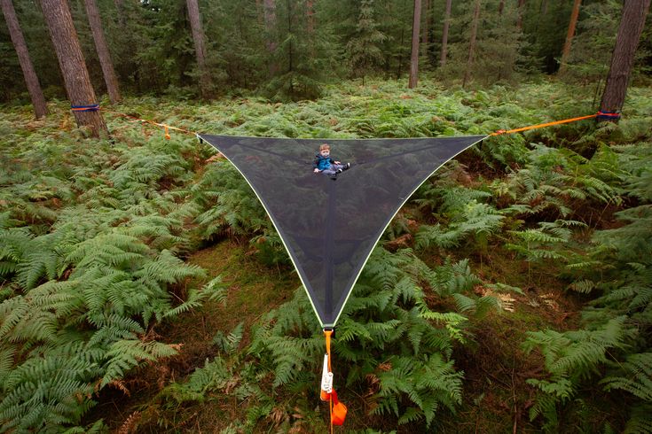 a man standing in the middle of a forest holding onto a tarp over his head