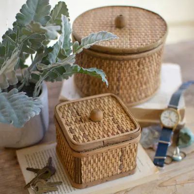 two wicker boxes with plants in them on top of a wooden table next to other items