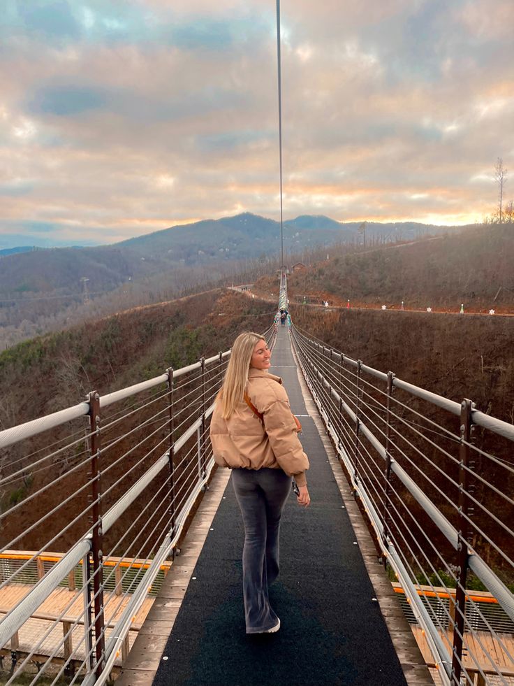 a woman is walking across a bridge with mountains in the backgrounds