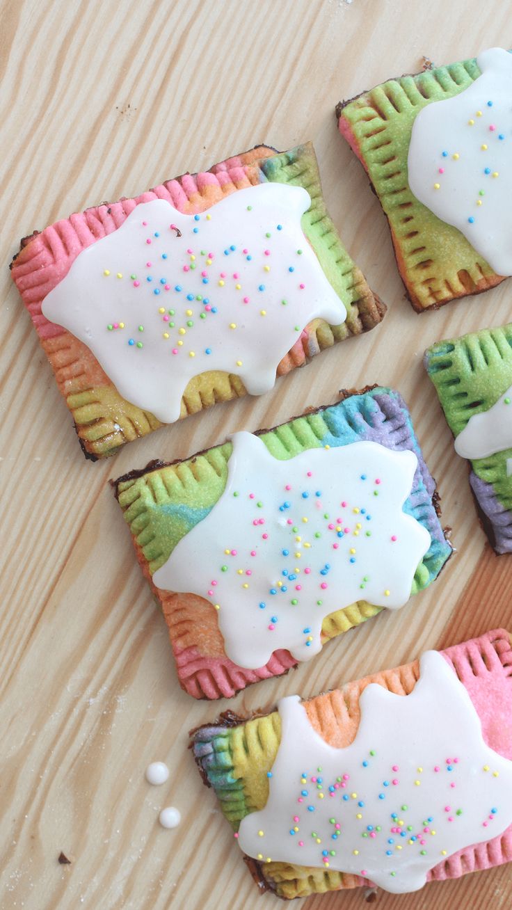 four decorated cookies sitting on top of a wooden table next to white frosting and sprinkles