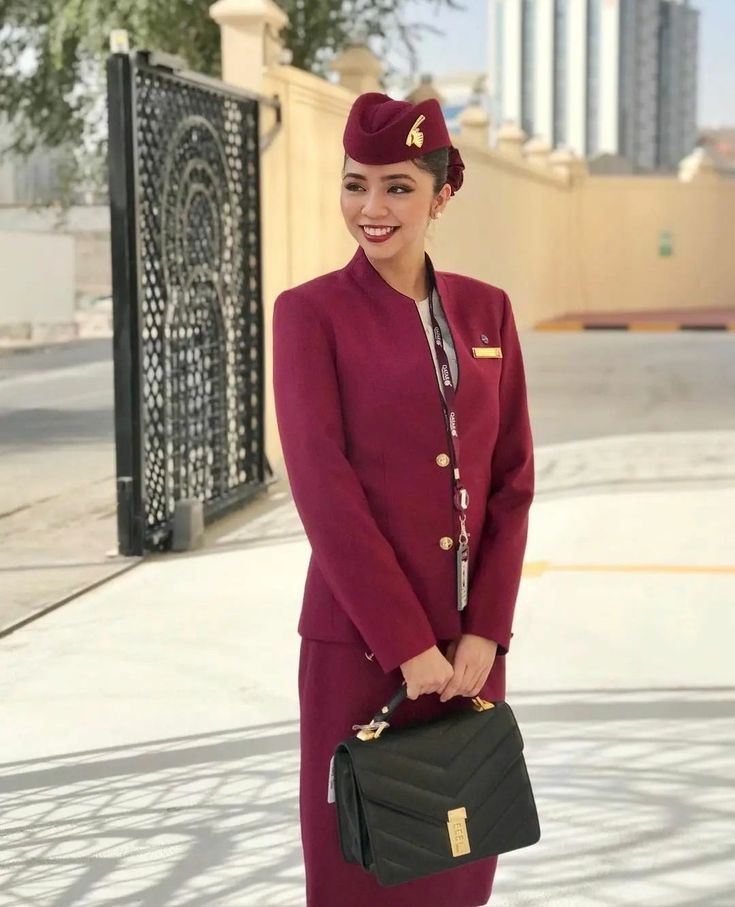 a woman in an air hostess uniform holding a black purse and smiling at the camera