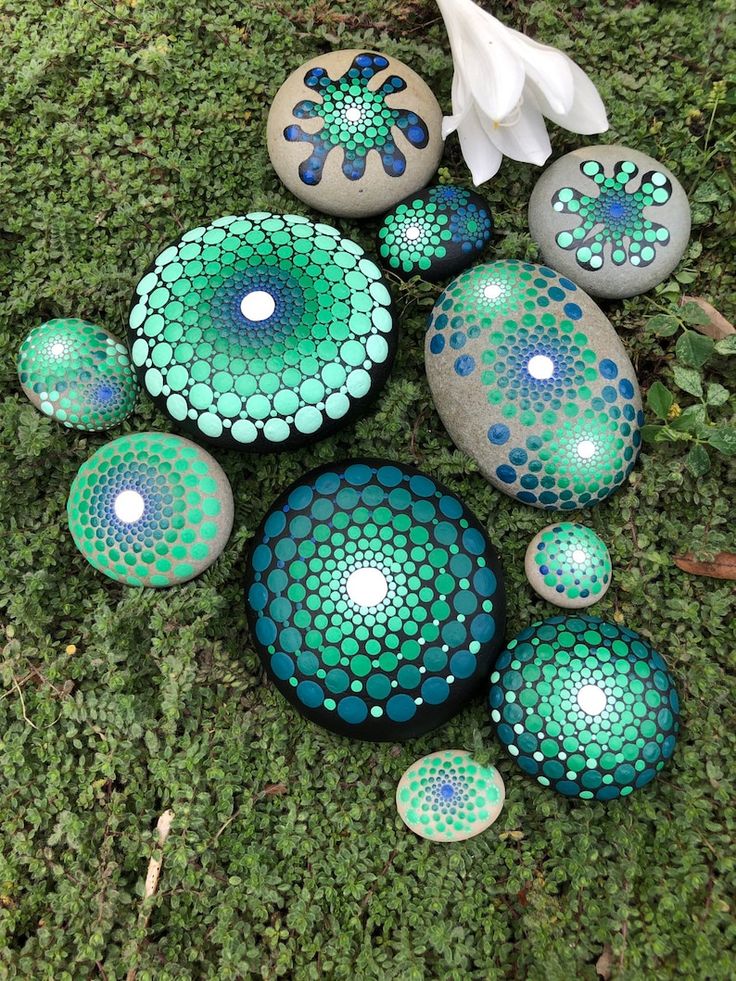 painted rocks sitting in the grass next to a white flower on top of green grass